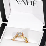 A gold engagement ring with a large round center stone and smaller accent stones, displayed inside an open white Vahé jewelry box.
