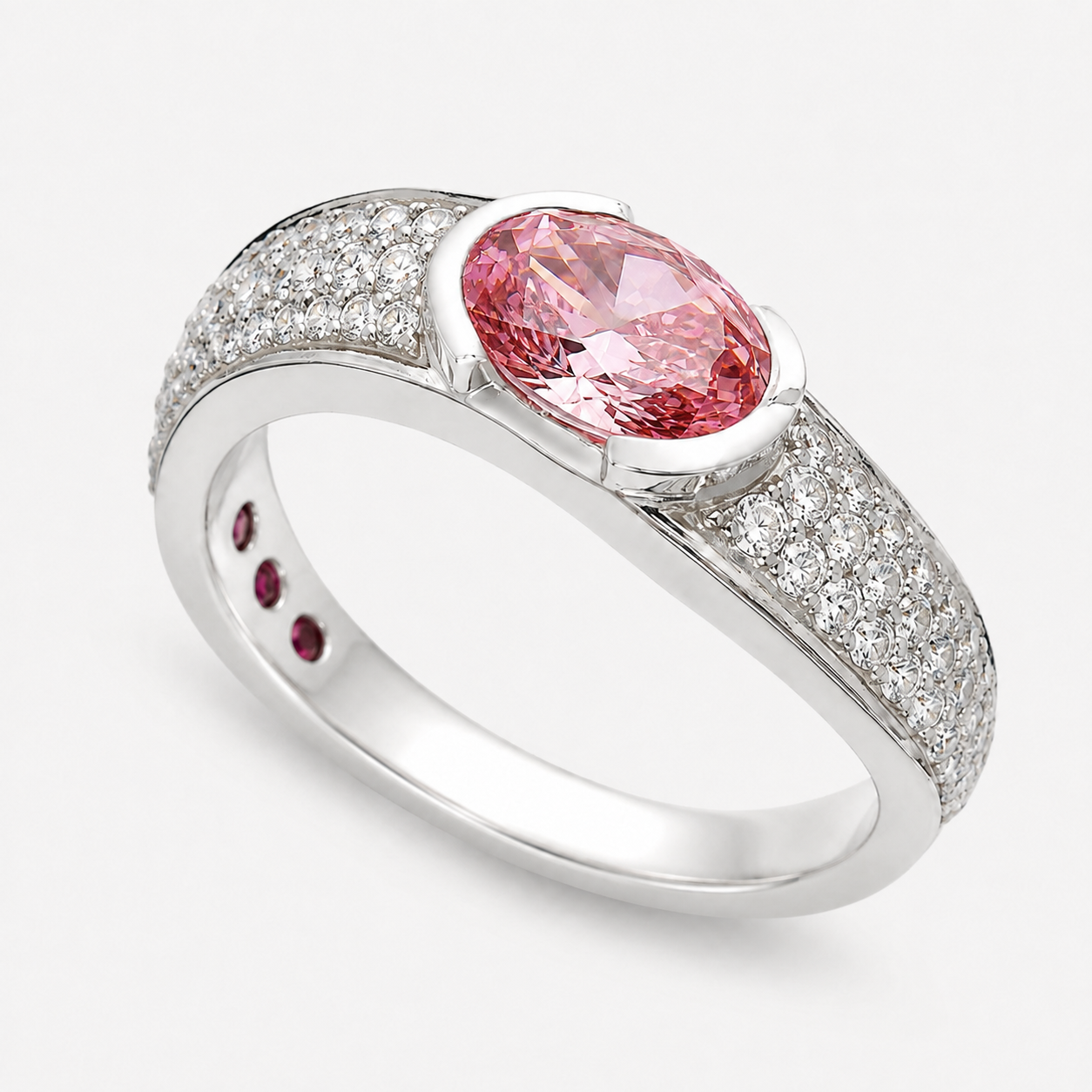 A silver-toned oval ring featuring a large pink gemstone, with pavé-set clear stones along the shoulders and three small round pink stones on the inner band, shown on a light gray background.
