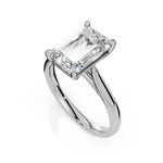 An emerald-cut diamond engagement ring in a polished silver-colored metal band, shown on a clean white background with a soft reflection.