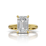 An emerald-cut diamond ring set in yellow gold, featuring a brilliant center stone and a polished shank, shown on a clean white background with a soft reflection below.