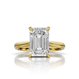 An emerald-cut diamond ring set in yellow gold, featuring a brilliant center stone and a polished shank, shown on a clean white background with a soft reflection below.