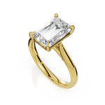 An emerald-cut diamond engagement ring in a polished yellow gold setting, shown on a clean white background with a soft reflection.