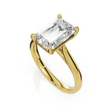 An emerald-cut diamond engagement ring in a polished yellow gold setting, shown on a clean white background with a soft reflection.