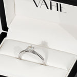 A low set round diamond solitaire with cathedral shoulders in 18ct white gold, displayed inside an open white VAHE ring box.
