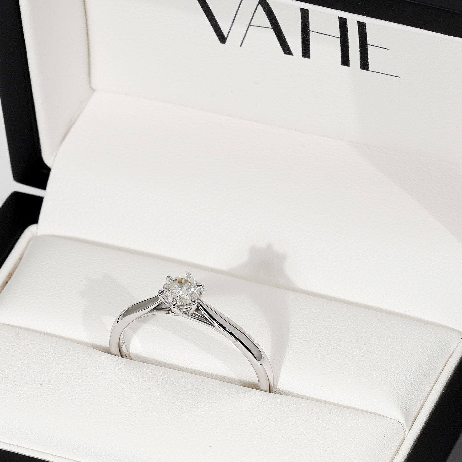 A low set round diamond solitaire with cathedral shoulders in 18ct white gold, displayed inside an open white VAHE ring box.