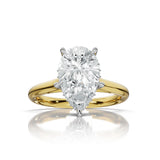 A pear-cut diamond solitaire engagement ring set in a yellow gold band with a silver-colored prong setting, shown on a clean white background with a soft reflection below.