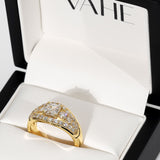 A gold ring with a diamond-encrusted geometric setting, displayed inside an open white jewelry box with the brand name VAHE visible on the inner lid.