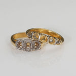 A gold ring with a three-stone cluster setting featuring clear round-cut gemstones and small diamond accents, photographed on a clean white reflective surface.