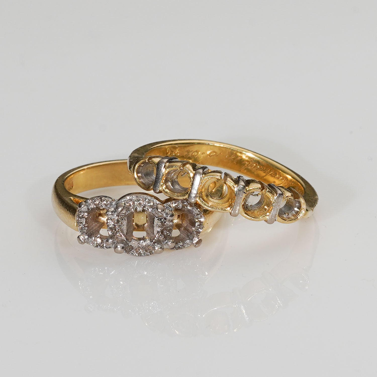 A gold ring with a three-stone cluster setting featuring clear round-cut gemstones and small diamond accents, photographed on a clean white reflective surface.