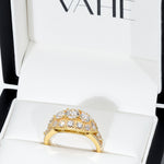A gold dome ring set with multiple round clear gemstones, displayed inside an open white jewelry box with the brand name VAHE visible on the inner lid.