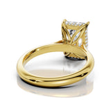 A yellow gold ring with a rectangular clear gemstone in a decorative openwork setting, shown on a clean white background with a soft reflection.
