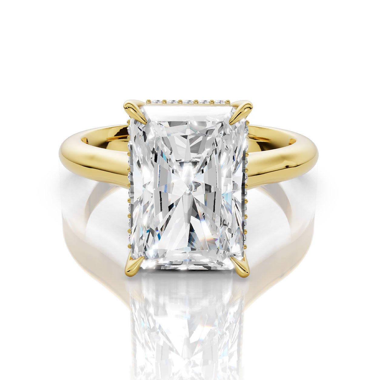 An emerald-cut diamond engagement ring with a yellow gold band and small diamond accents on the shoulders, shown on a reflective white surface.