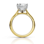 A yellow gold diamond ring with a brilliant round-cut center stone and small accent diamonds in a silver-colored setting, shown on a clean white background with a soft reflection below.